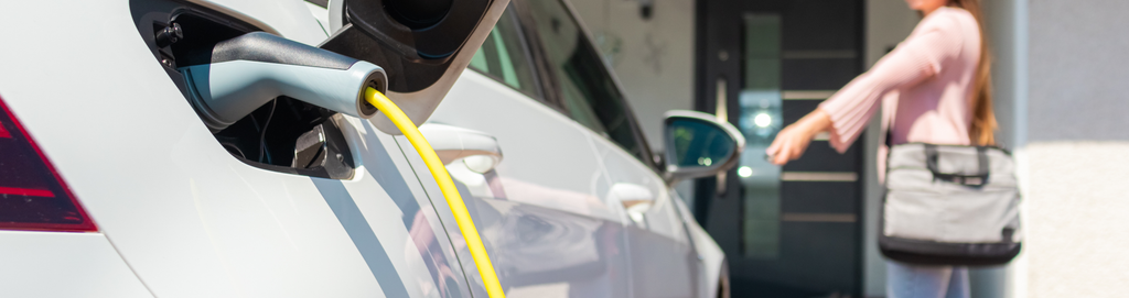 close of a car being charged while in the background there is a blurred women locking the vehicle.