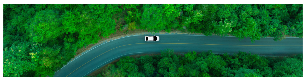 Top view of a white electric car driving along an elevated road surrounded by a dense, dark green forest. This image highlights the concept of using electric vehicles for eco-friendly transportation and environmental protection.