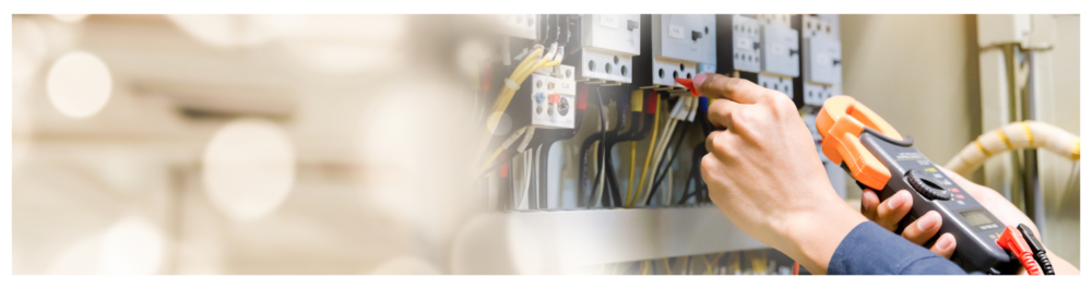 An electrician engineer uses a tester to measure voltage and current in a power electric line within an electrical control cabinet.