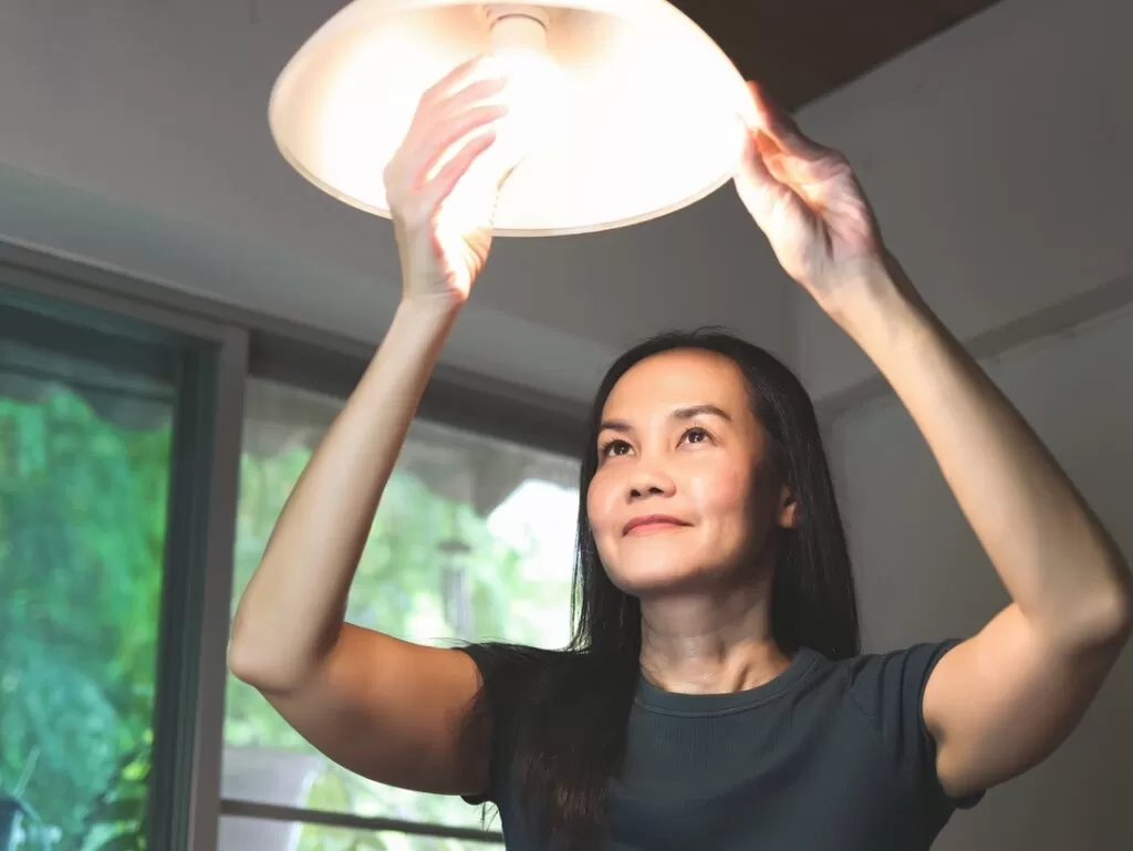 Homeowner changing light bulb to represent task that does not require electrical permit