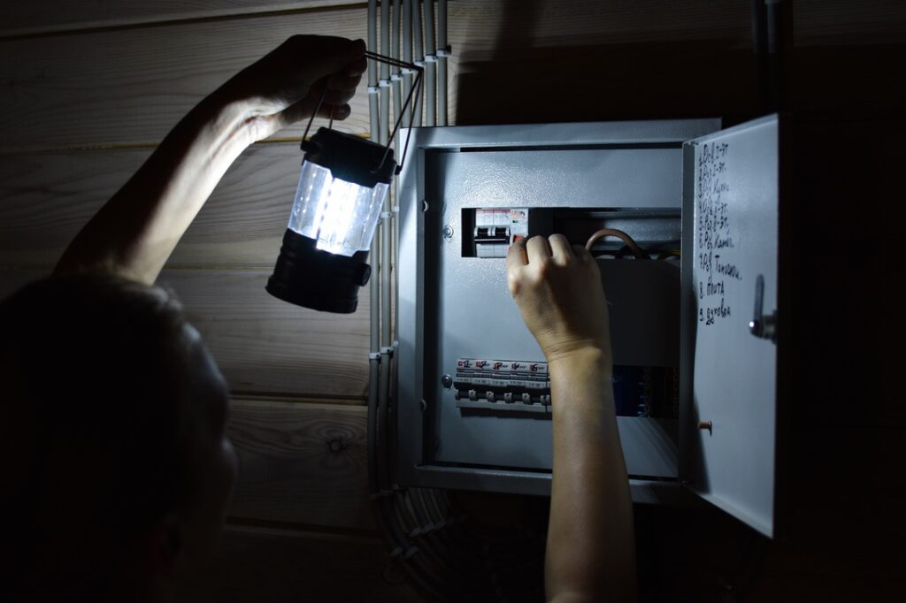 Homeowner with lamp checking electrical panel after power outage due to overload