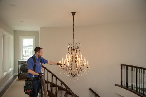Worker inspects wiring on chandelier hanging in home.