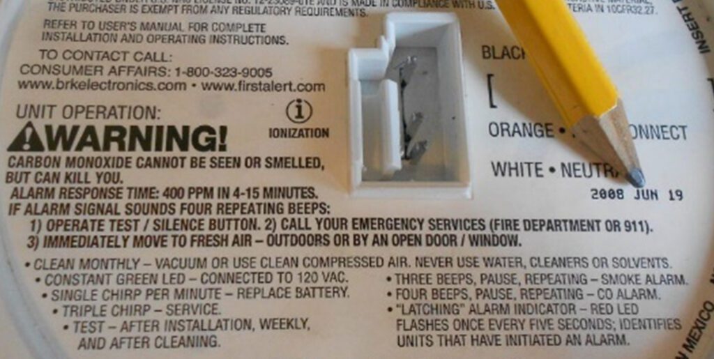 Closeup of back of smoke detector with pencil pointing to expiration date.