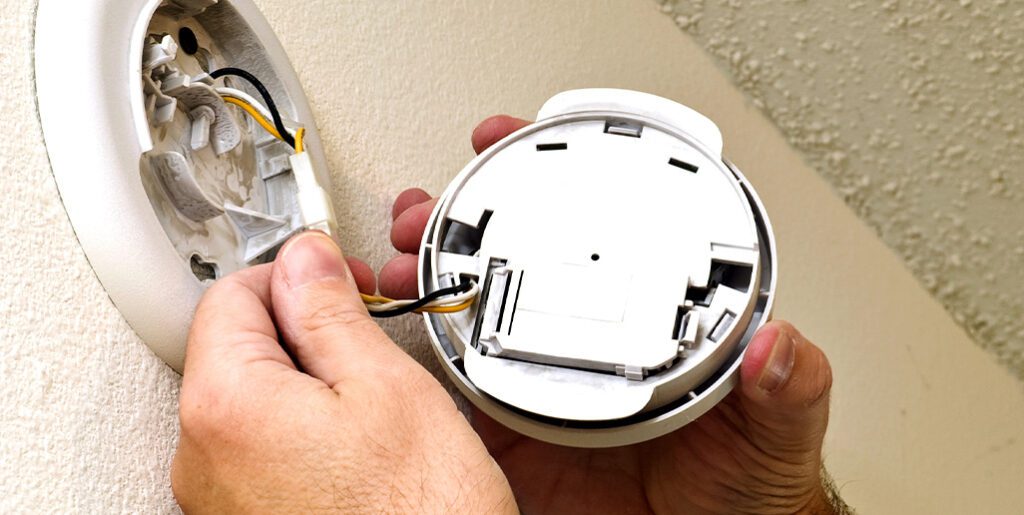 Man inspects wiring on smoke alarm.