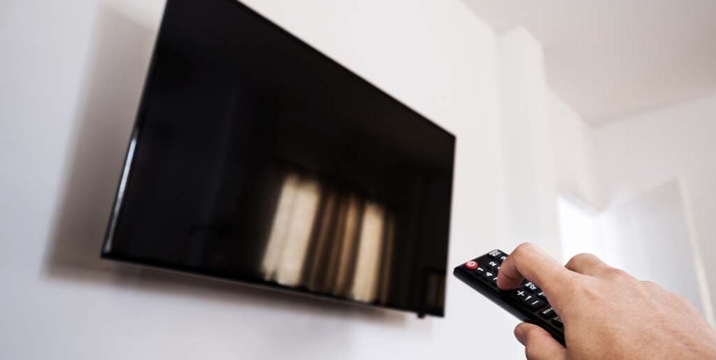 Person holding remote turning off flat screen TV.