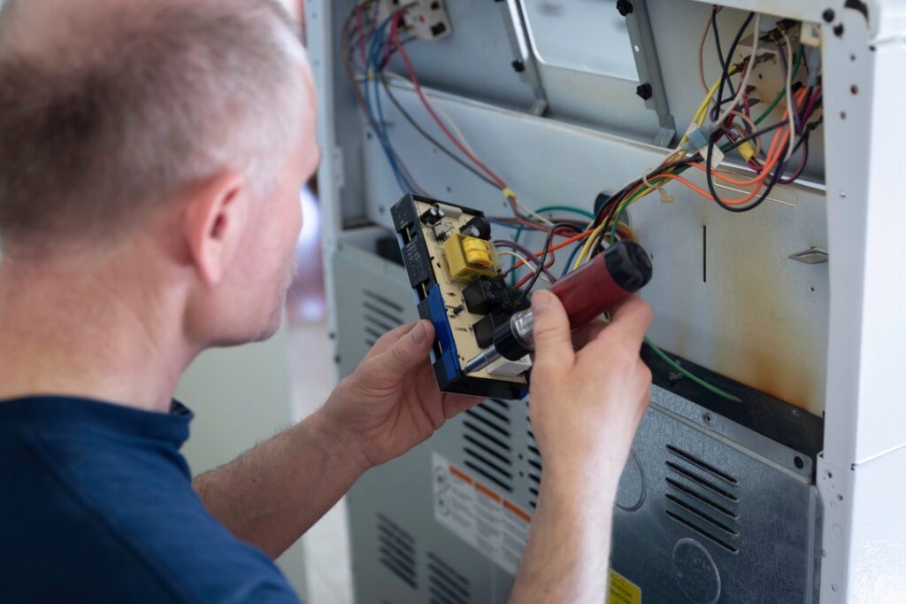 horizontal close up image  of a caucasian  adult male fixing the panel attaching wires at the back of an electric stove.