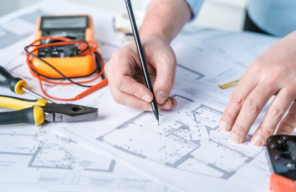 Man repairer making electricity project in house.Repairs planning.Drawing,diagrams,plan of electrification of apartment,building.Devices,accessories,voltmeter,wires,screwdriver,pliers and tape measure