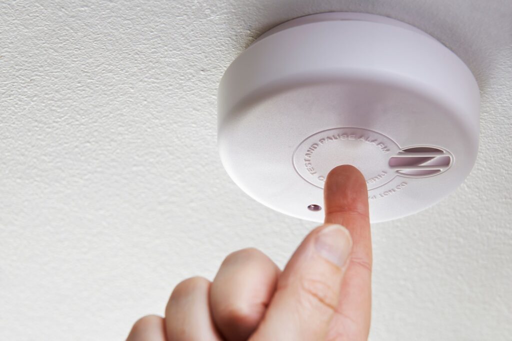 Person testing smoke and carbon monoxide detectors at home