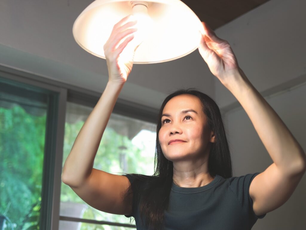Homeowner changing light bulb to represent task that does not require electrical permit