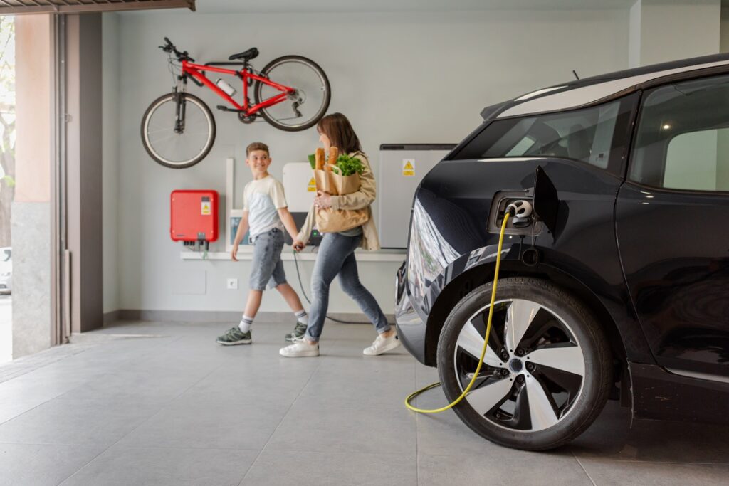 Mother and son walking out of garage with home EV charger plugged into electric vehicle nearby
